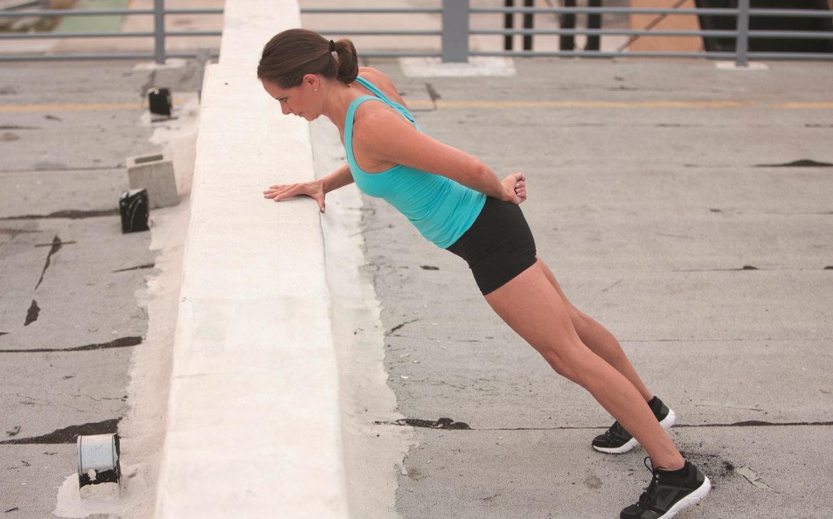 A woman performing a press exercise outdoors against a wall